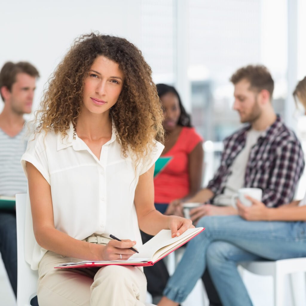 focused woman writing while colleagues are talking behind her in creative office